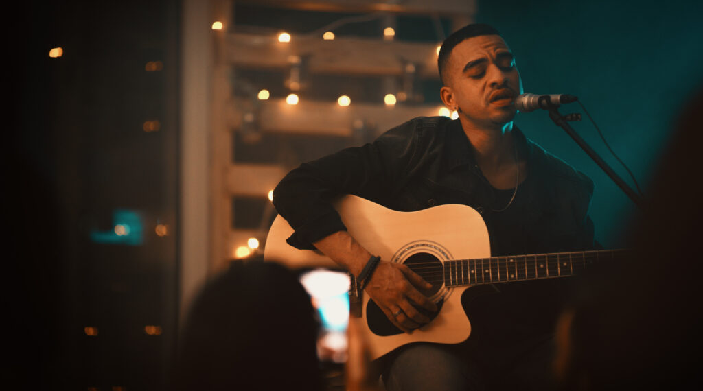 Shot of a young man singing and playing the guitar on stage