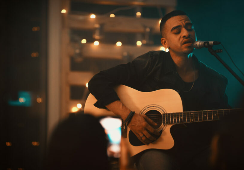 Shot of a young man singing and playing the guitar on stage