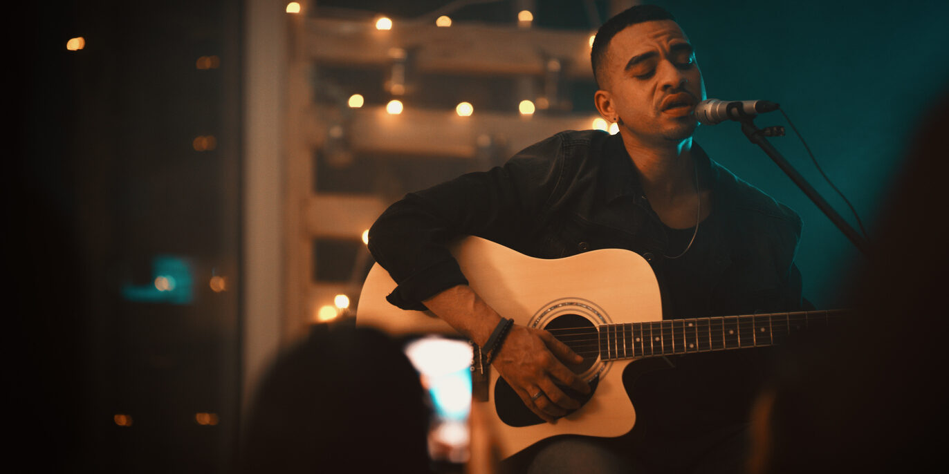 Shot of a young man singing and playing the guitar on stage