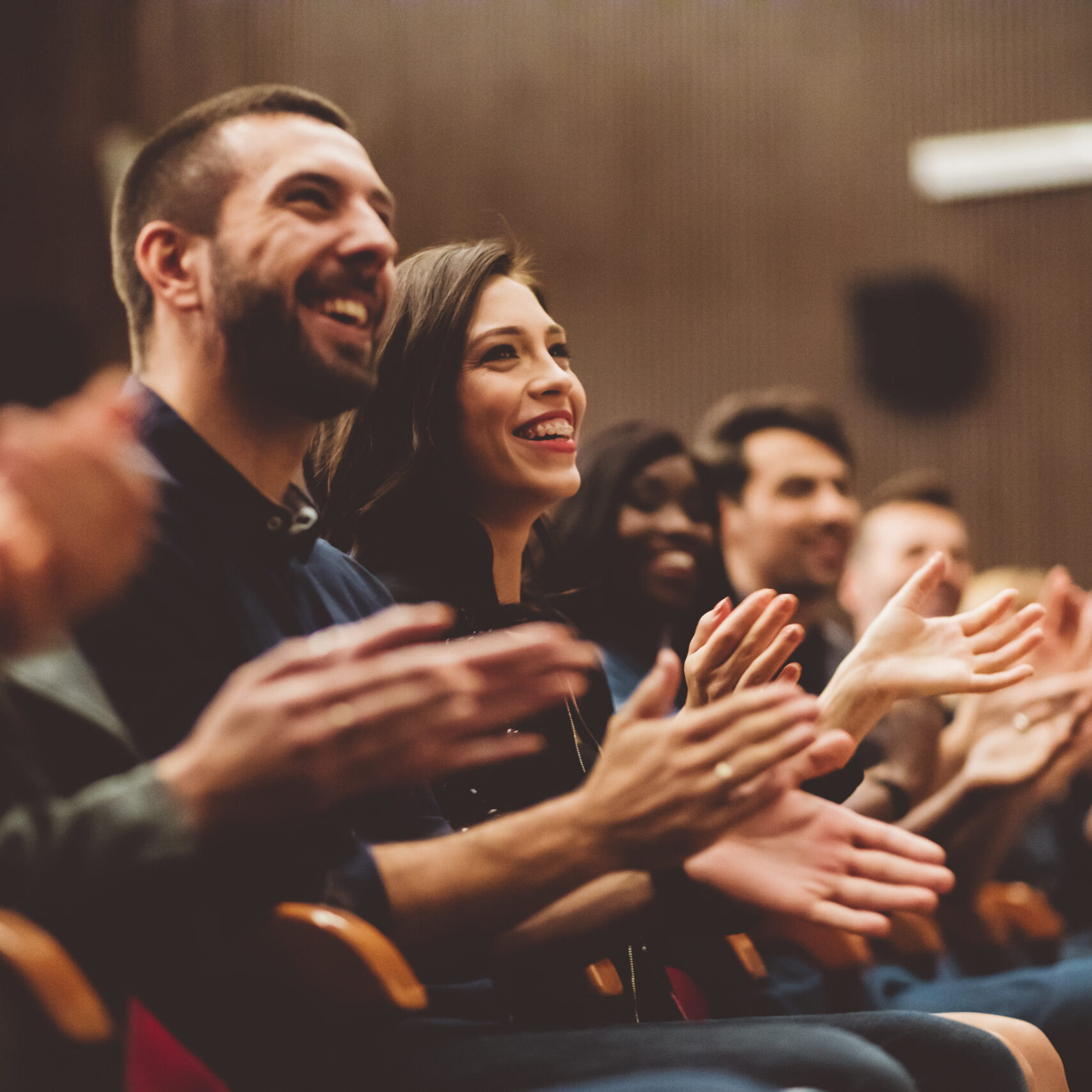 Group of smiling people clapping hands in the theater, close up of hands. Dark tone.