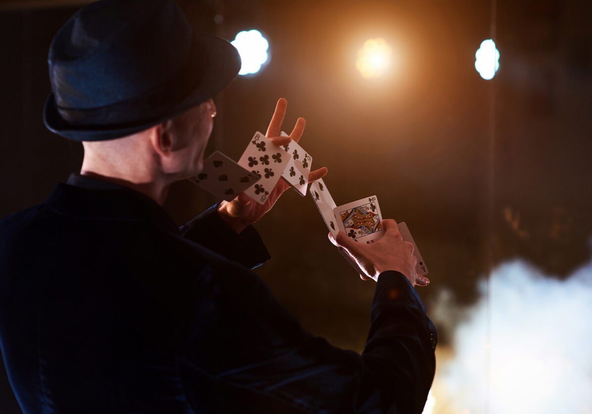 Magician showing trick with playing cards. Magic or dexterity, circus, gambling. Prestidigitator in dark room with fog Magician showing trick with playing cards. Magic or dexterity, circus, gambling. Prestidigitator in dark room with fog.