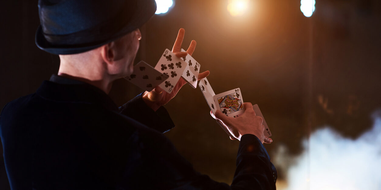 Magician showing trick with playing cards. Magic or dexterity, circus, gambling. Prestidigitator in dark room with fog.